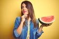 Young beautiful woman eating fresh healthy watermelon slice over yellow background serious face thinking about question, very Royalty Free Stock Photo