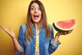 Young beautiful woman eating fresh healthy watermelon slice over yellow background very happy and excited, winner expression Royalty Free Stock Photo