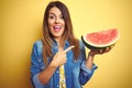 Young beautiful woman eating fresh healthy watermelon slice over yellow background very happy pointing with hand and finger Royalty Free Stock Photo