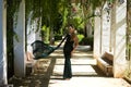 Young beautiful woman in elegant dress poses for photo among vines hanging from the columns in the park. The woman is happy and Royalty Free Stock Photo