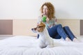 Young beautiful woman enjoying a healthy green detox juice on bed. Cute small dog besides. Lifestyle, indoors Royalty Free Stock Photo