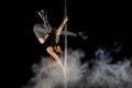 Young and beautiful woman exercises pole dance in the smoke against a black background Royalty Free Stock Photo