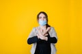 Young beautiful woman in face medical mask shows no jesture, bright yellow background.