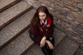 Young beautiful woman in a fashionable knitted vintage sweater in leather pants with a plaid scarf is sitting in the city on a Royalty Free Stock Photo