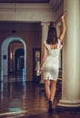 Young and beautiful woman girl white dress is in the palace, is standing near of pillar in style baroque Royalty Free Stock Photo