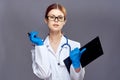 Young beautiful woman in glasses on a gray background holds a folder with documents and pen, doctor, medicine Royalty Free Stock Photo