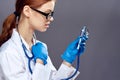 Young beautiful woman on a gray background with glasses and medical clothes holds a stethoscope and syringe, medicine, doctor Royalty Free Stock Photo