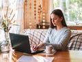 Young beautiful woman in a grey cozy sweater works for a computer from a home with a laptop on a wooden desk as a Royalty Free Stock Photo