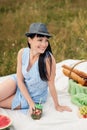 A young beautiful woman in hat and dress is drinking lemonade from a glass jar, sitting on plaid on green grass. Picnic Royalty Free Stock Photo