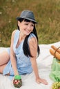 A young beautiful woman in hat and dress is drinking lemonade from a glass jar, sitting on plaid on green grass. Picnic Royalty Free Stock Photo