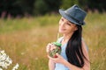 A young beautiful woman in hat and dress is drinking lemonade from a glass jar, sitting on plaid on green grass. Picnic Royalty Free Stock Photo