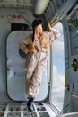 Young woman in a pilot`s suit stands at the opened door inside a plane Royalty Free Stock Photo