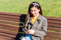 Young beautiful woman hipster cheerfully smiling and texting via smartphone sitting on bench in park in spring Royalty Free Stock Photo