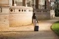 Young beautiful woman, Hispanic, brown hair, wearing striped sweater, linen pants and sunglasses, walking with her suitcase at Royalty Free Stock Photo