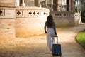 Young beautiful woman, Hispanic, brown hair, wearing striped sweater, linen pants, walking with her suitcase at sunset, back view Royalty Free Stock Photo