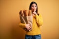 Young beautiful woman holding a bag of fresh healthy bread over yellow background asking to be quiet with finger on lips Royalty Free Stock Photo