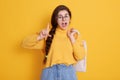 Young beautiful woman holding bag over yellow background, gesturing with hand doing small size sign with fingers, looking at Royalty Free Stock Photo