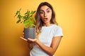 Young beautiful woman holding basil pot over yellow isolated background scared in shock with a surprise face, afraid and excited Royalty Free Stock Photo