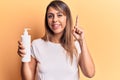 Young beautiful woman holding bottle of cream lotion smiling with an idea or question pointing finger with happy face, number one Royalty Free Stock Photo