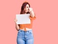 Young beautiful woman holding cardboard banner with blank space pointing with finger to the camera and to you, confident gesture Royalty Free Stock Photo