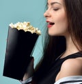 Young beautiful woman holding eating popcorn over mint background