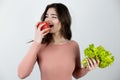 Young beautiful woman holding green salad in one hand and biting fresh apple in another looking happy being on diet isolated white Royalty Free Stock Photo