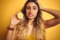 Young beautiful woman holding half lemon over yellow isolated background stressed with hand on head, shocked with shame and