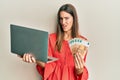 Young beautiful woman holding laptop and 50 euros in shock face, looking skeptical and sarcastic, surprised with open mouth Royalty Free Stock Photo