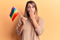 Young beautiful woman holding lgtbq flag covering mouth with hand, shocked and afraid for mistake