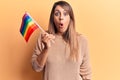 Young beautiful woman holding lgtbq flag scared and amazed with open mouth for surprise, disbelief face