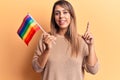 Young beautiful woman holding lgtbq flag smiling happy pointing with hand and finger to the side