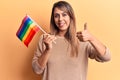 Young beautiful woman holding lgtbq flag smiling happy and positive, thumb up doing excellent and approval sign