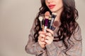 Young beautiful woman holding makeup brushes in her hands and posing on grey background at studio Royalty Free Stock Photo