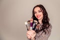 Young beautiful woman holding makeup brushes in her hands and posing on grey background at studio Royalty Free Stock Photo