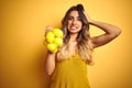 Young beautiful woman holding net of lemons over yellow  background stressed with hand on head, shocked with shame and Royalty Free Stock Photo