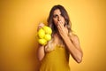 Young beautiful woman holding net of lemons over yellow isolated background cover mouth with hand shocked with shame for mistake, Royalty Free Stock Photo