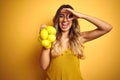 Young beautiful woman holding net of lemons over yellow isolated background with happy face smiling doing ok sign with hand on eye Royalty Free Stock Photo