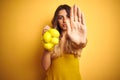 Young beautiful woman holding net of lemons over yellow isolated background with open hand doing stop sign with serious and Royalty Free Stock Photo