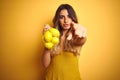 Young beautiful woman holding net of lemons over yellow isolated background pointing with finger to the camera and to you, hand Royalty Free Stock Photo