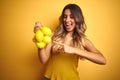 Young beautiful woman holding net of lemons over yellow isolated background very happy pointing with hand and finger Royalty Free Stock Photo