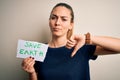 Young beautiful woman holding paper asking for save earth and enviroment conservation with angry face, negative sign showing