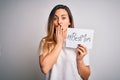 Young beautiful woman holding paper with best mom message celebrating mothers day cover mouth with hand shocked with shame for