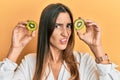 Young beautiful woman holding slice of kiwi over eyes clueless and confused expression Royalty Free Stock Photo