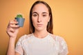 Young beautiful woman holding small cactus plant pot over  yellow background with a confident expression on smart face Royalty Free Stock Photo