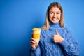 Young beautiful woman holding take away glass of coffee over isolated blue background happy with big smile doing ok sign, thumb up Royalty Free Stock Photo