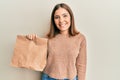 Young beautiful woman holding take away paper bag looking positive and happy standing and smiling with a confident smile showing Royalty Free Stock Photo