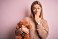 Young beautiful woman holding teddy bear standing over isolated pink background cover mouth with hand shocked with shame for Royalty Free Stock Photo