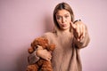 Young beautiful woman holding teddy bear standing over isolated pink background pointing with finger to the camera and to you, Royalty Free Stock Photo