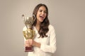 Young beautiful woman holding trophy over grey background. Woman holding a trophy. Successful employee holds winner cup Royalty Free Stock Photo