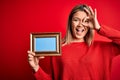 Young beautiful woman holding vintage frame standing over isolated red background with happy face smiling doing ok sign with hand Royalty Free Stock Photo